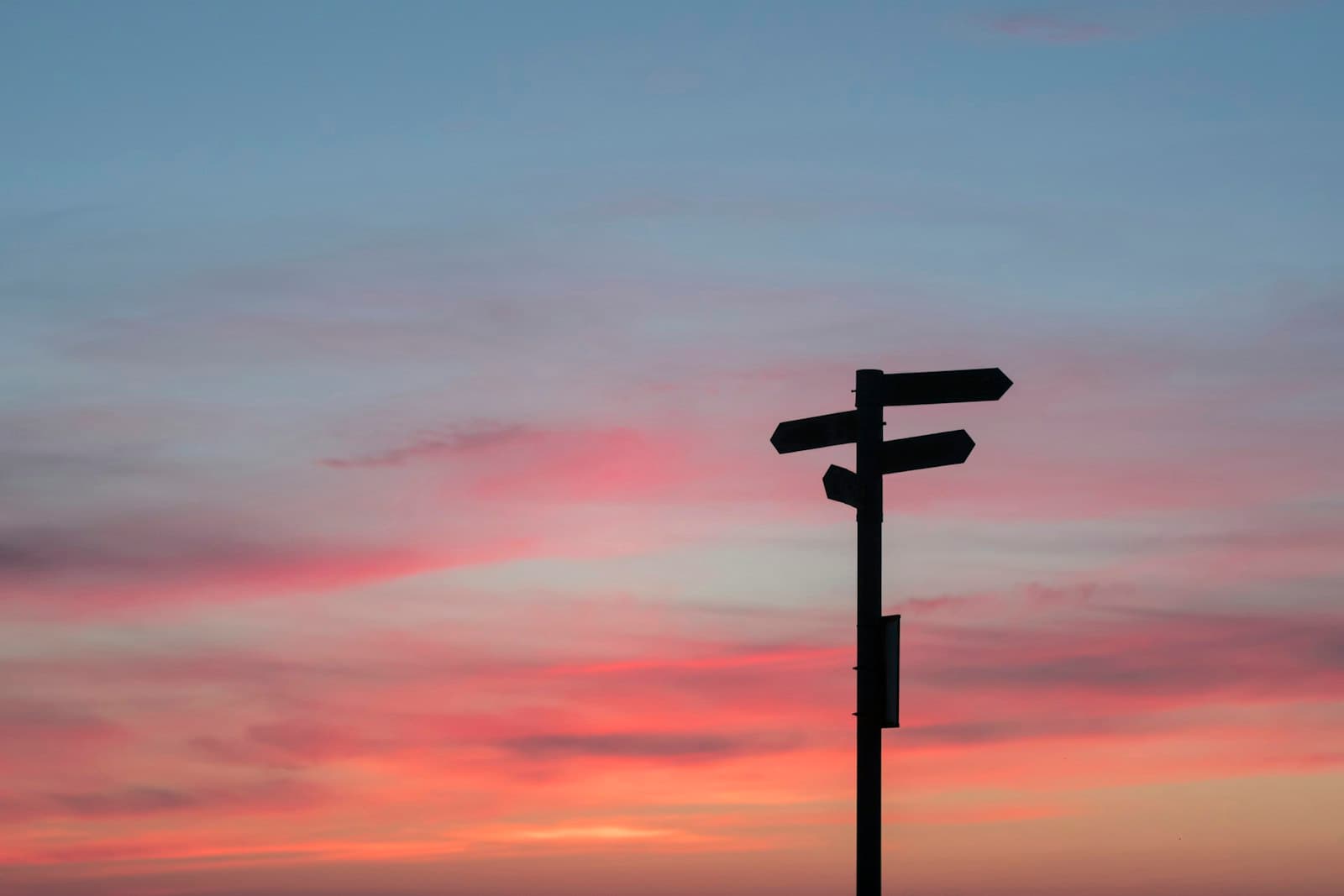 A silhouetted signpost with arms pointing in different directions against a sunset sky.