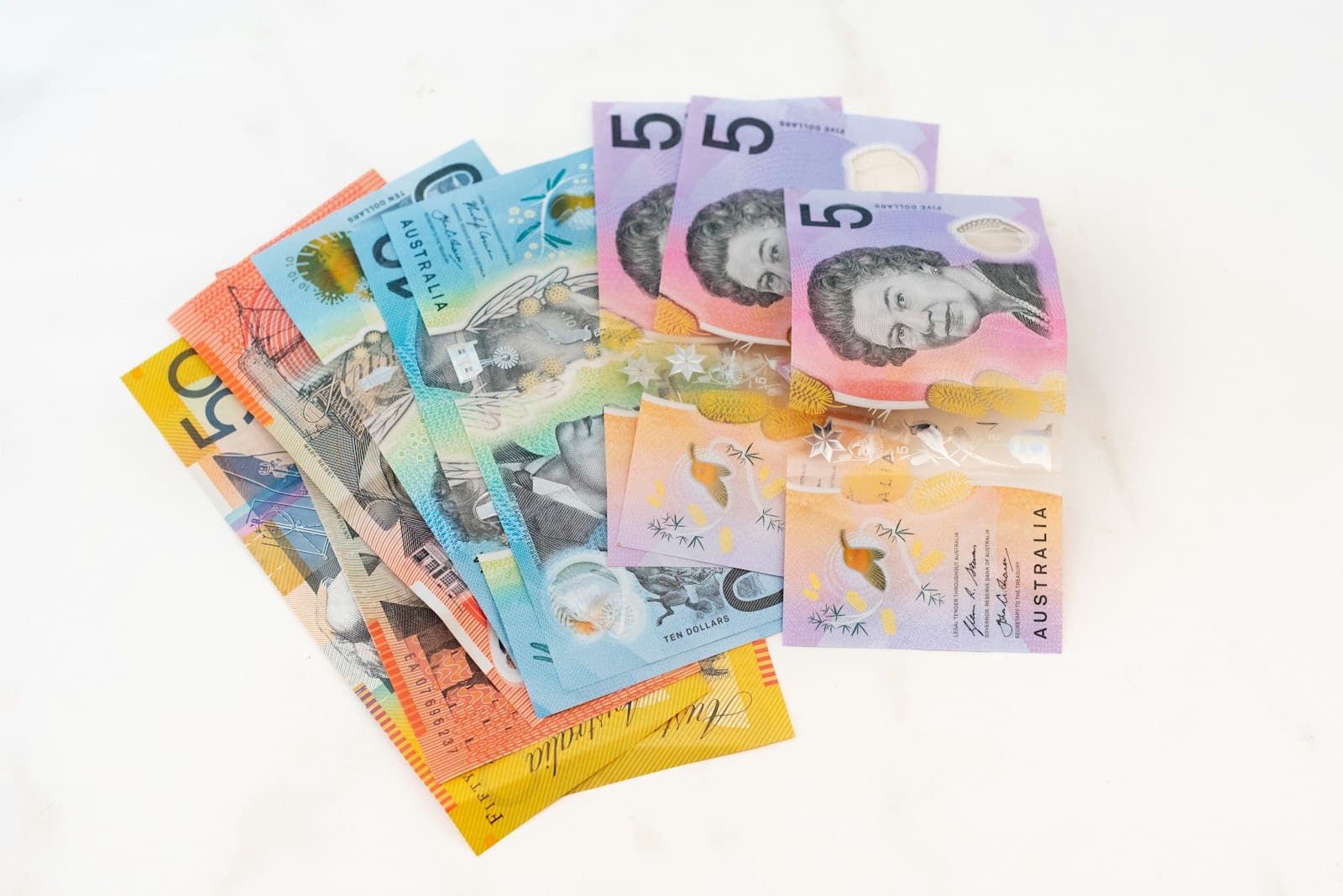 A fan of Australian banknotes of assorted denominations on a white surface.