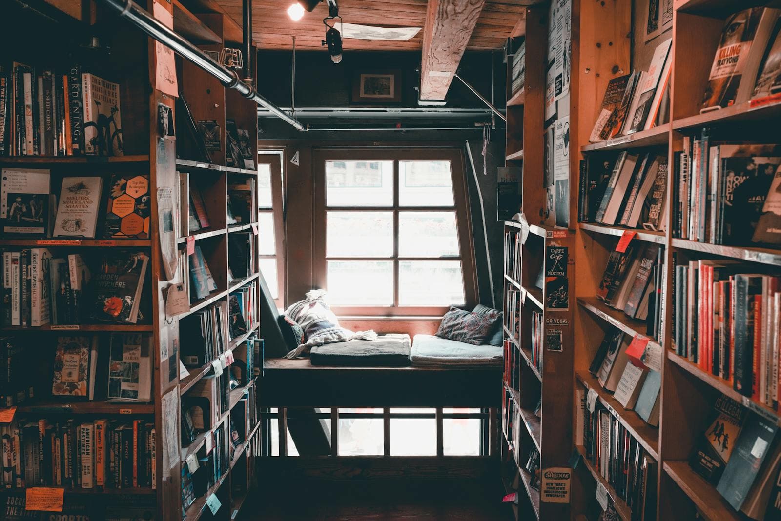 A cosy bookshop corner with tall shelves and a reading nook by a window.