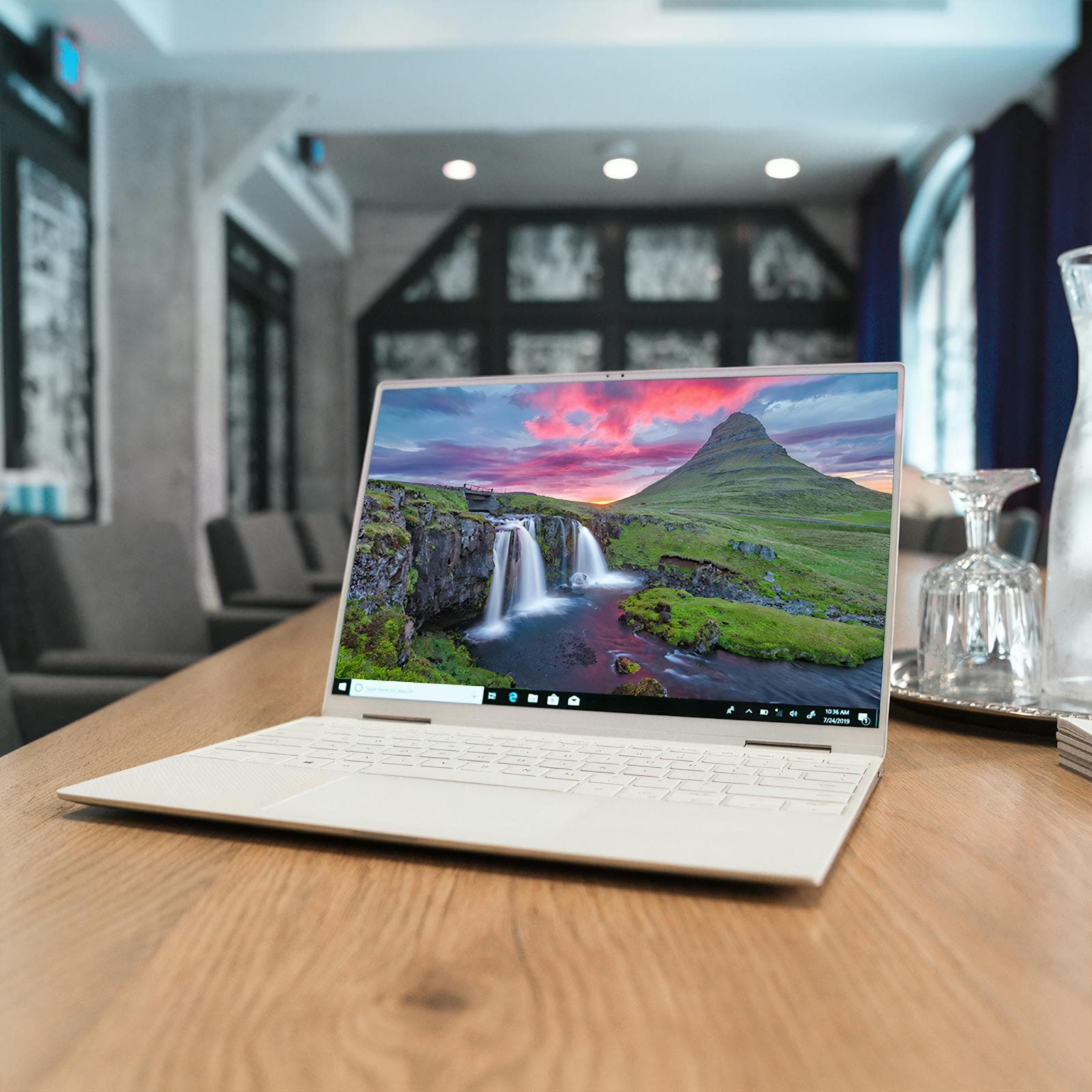 A laptop open on a long meeting table in a bright room.