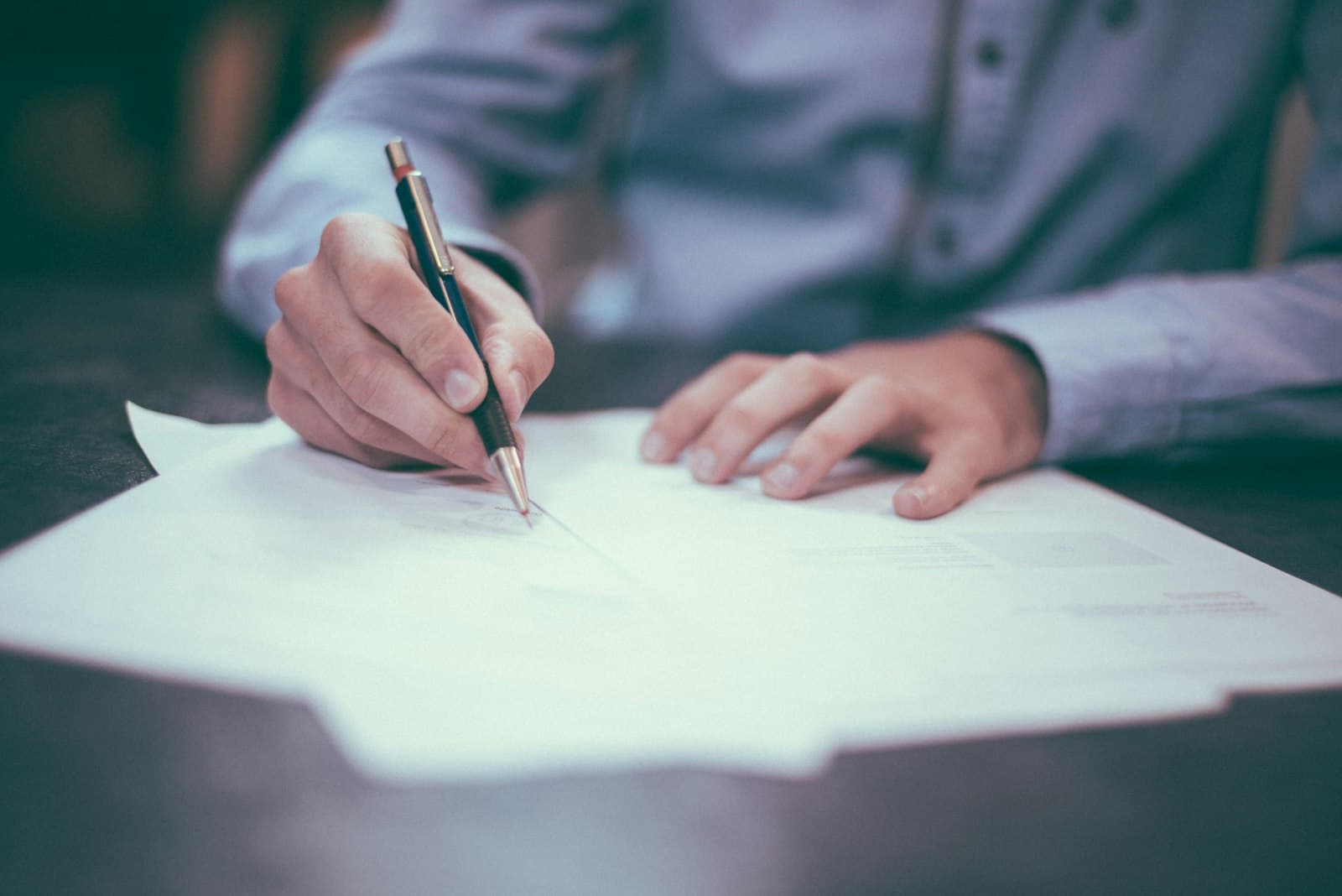A person working through paperwork at a desk with a pen.