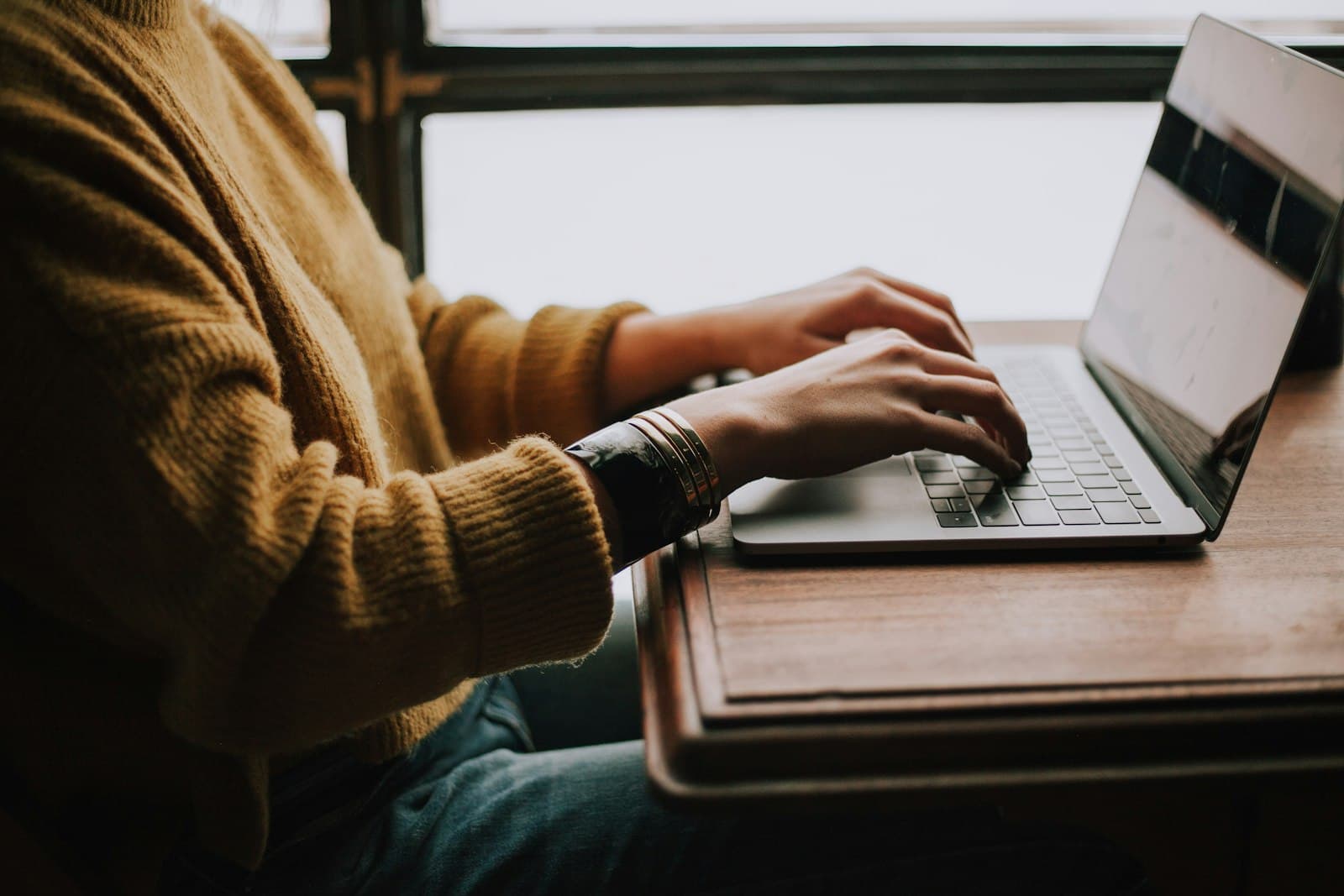 A person at a window desk typing on a laptop, reviewing their monthly savings pace.