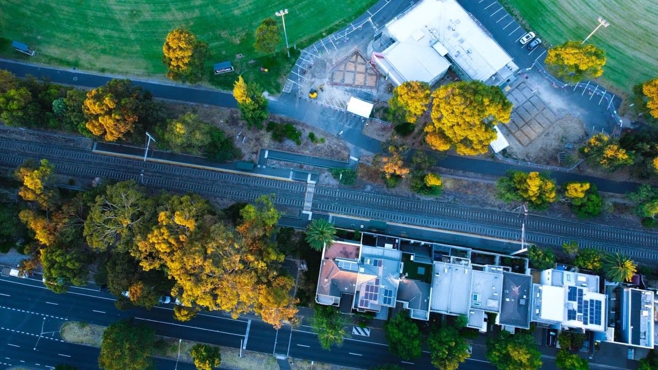 Aerial view of a row of Australian homes beside a tree-lined street and railway line.