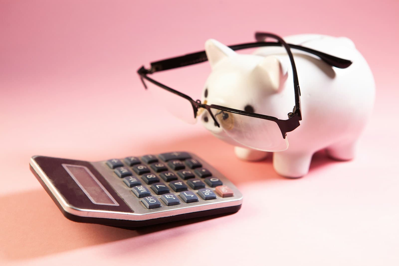 A piggy bank wearing reading glasses beside a calculator, for weighing up offset savings.