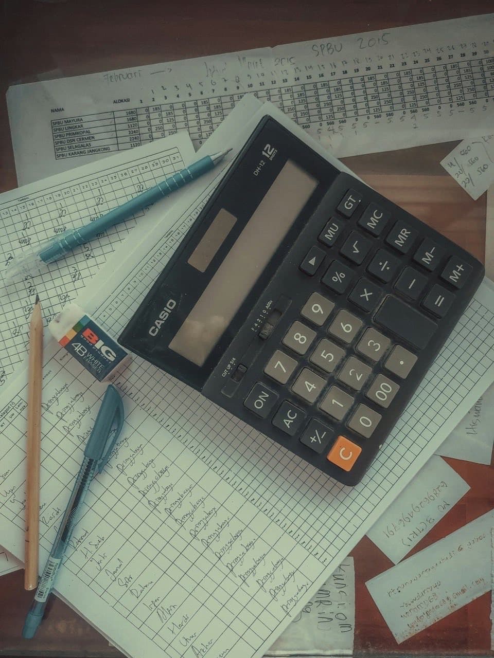A desktop calculator sitting on handwritten worksheets of figures.