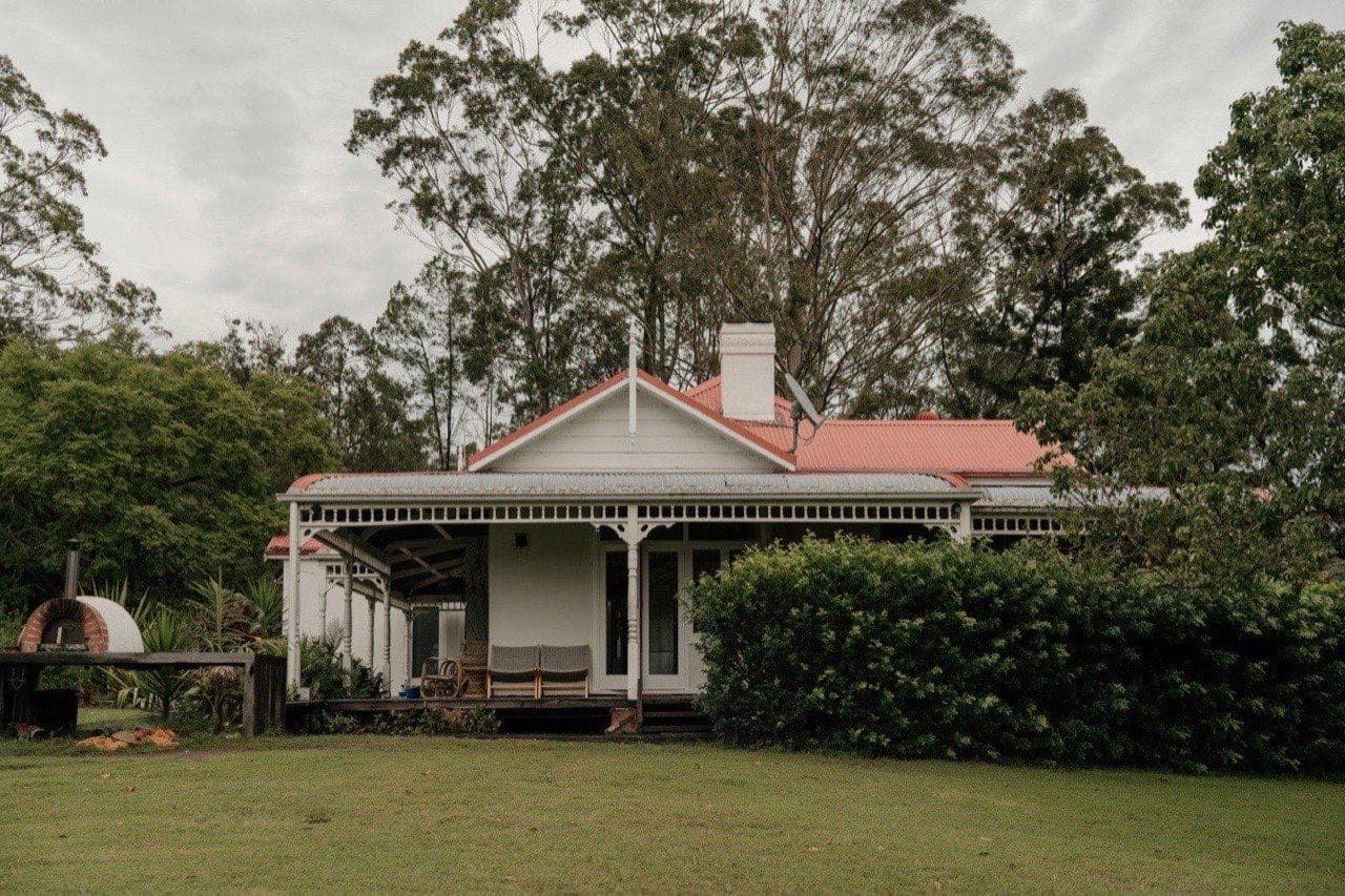A traditional Australian house with a red roof and wide veranda, surrounded by established gum trees.