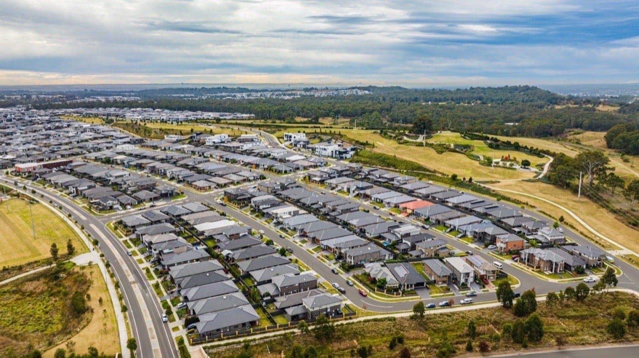 Aerial view of an Australian suburban estate with rows of new houses along curving streets.