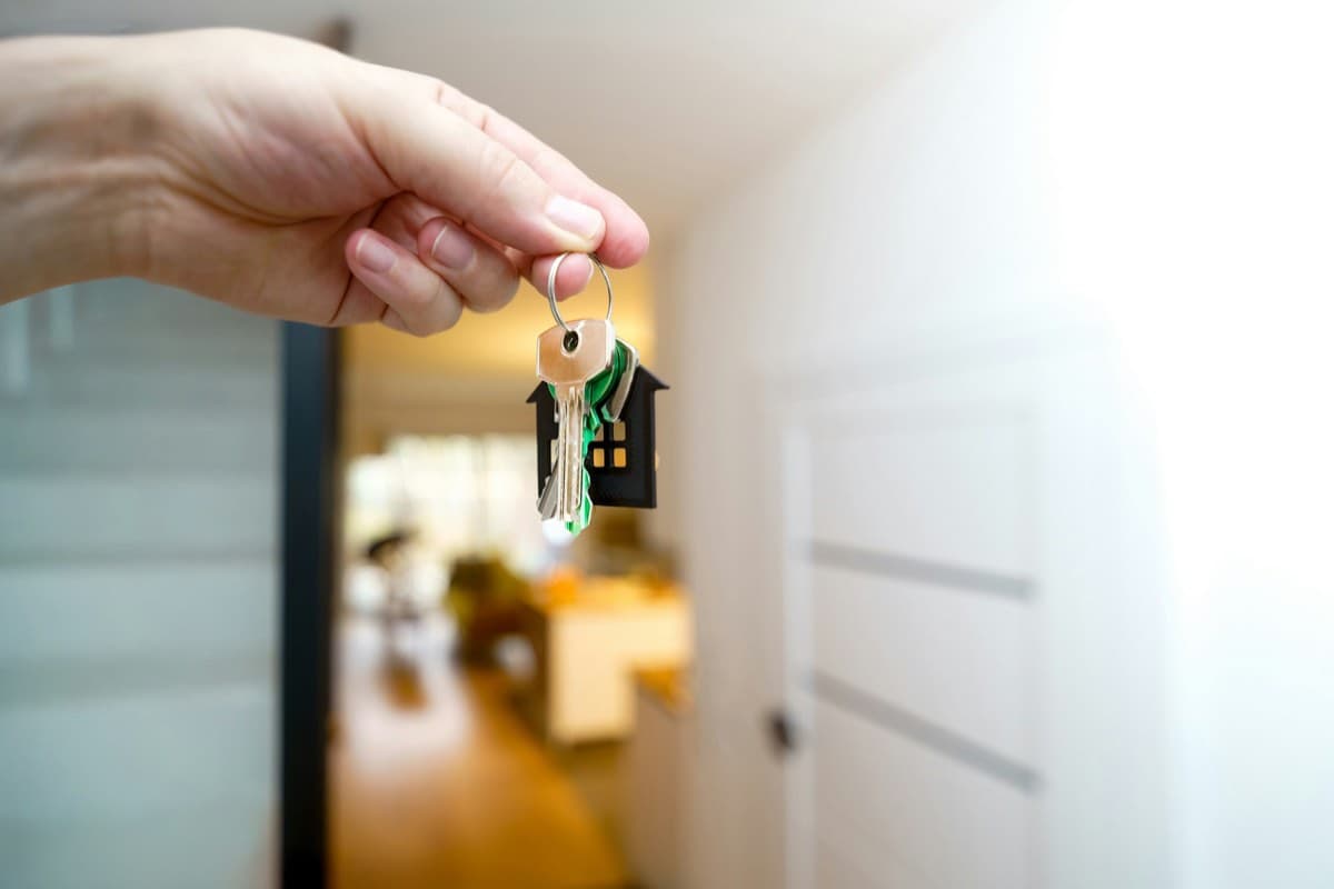 A hand holding house keys in front of a home's entrance.