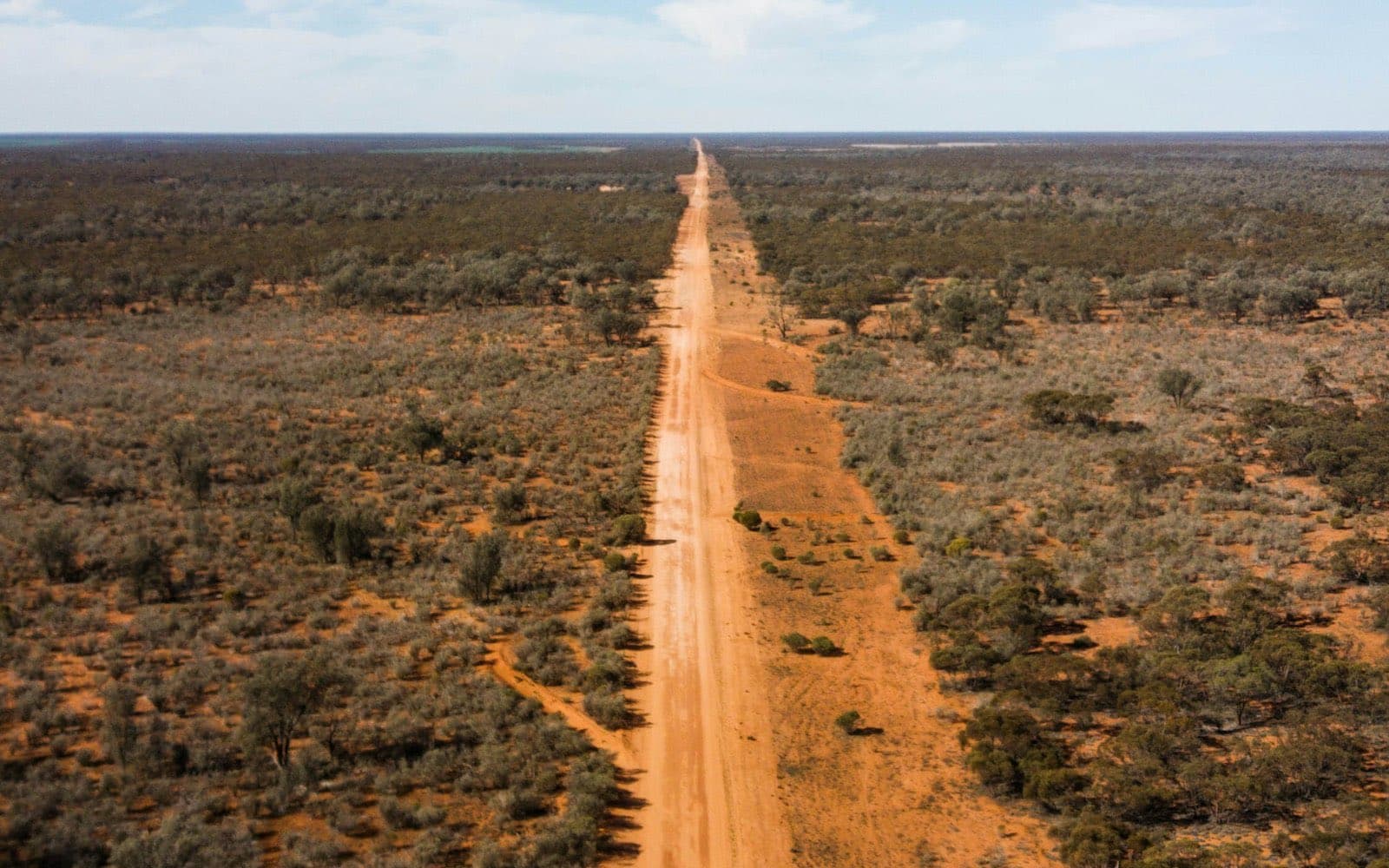 A long straight outback road stretching to the horizon under a blue sky.