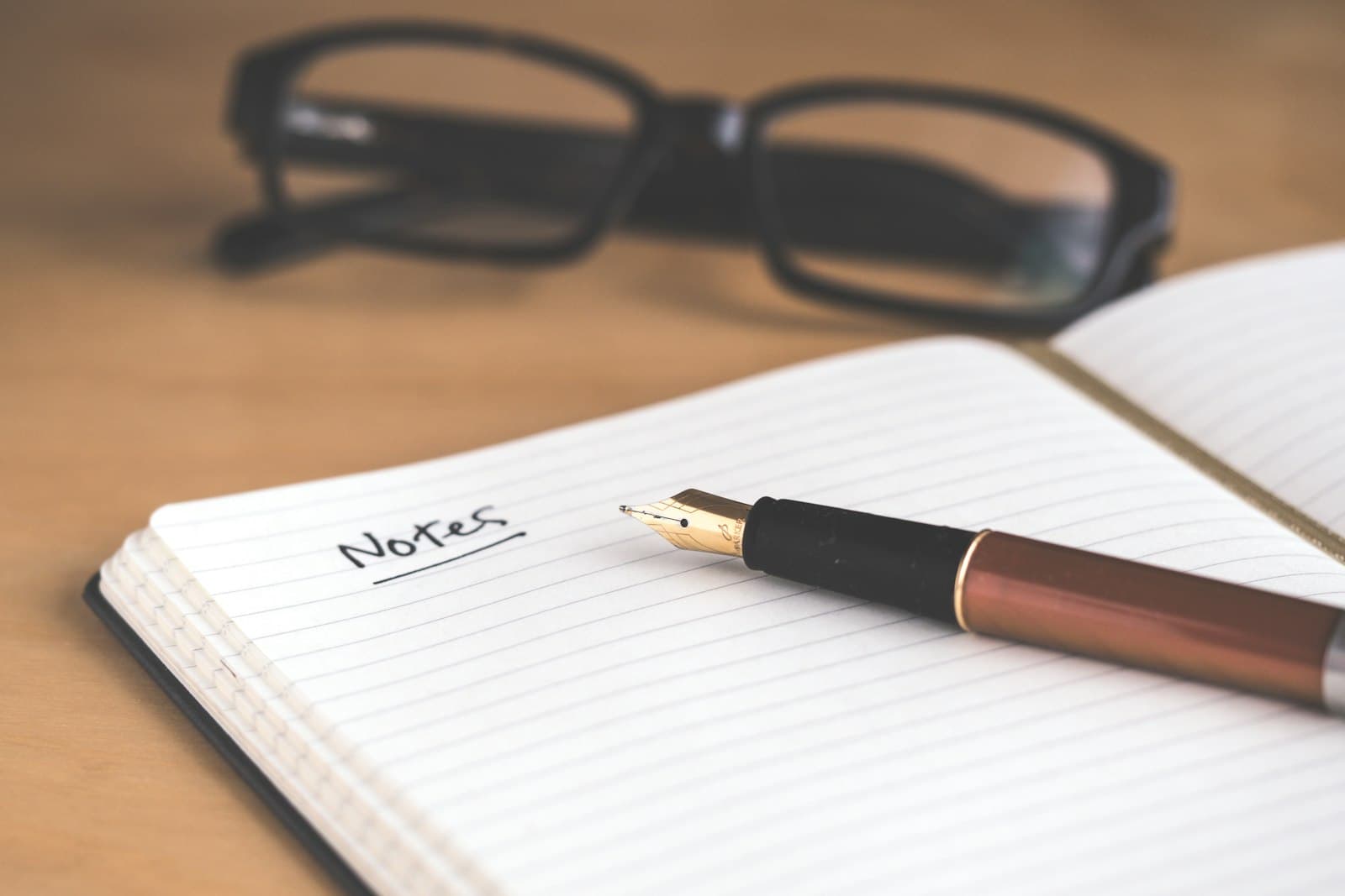 An open notebook headed Notes with a fountain pen resting on it and glasses in the background.