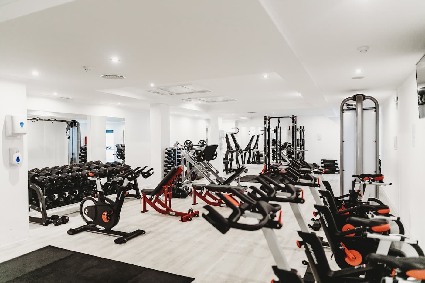 An empty gym with rows of unused spin bikes and weight equipment.