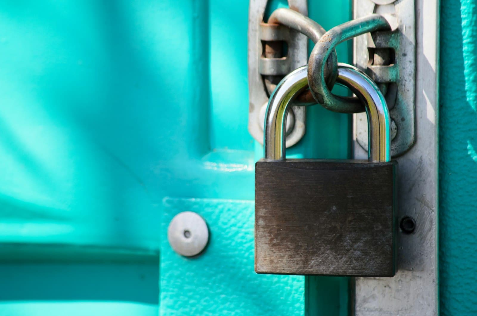 A close-up of a steel padlock securing a teal door.