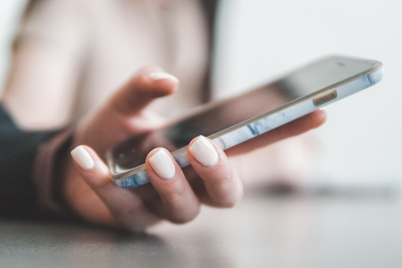 A hand holding a smartphone above a desk.