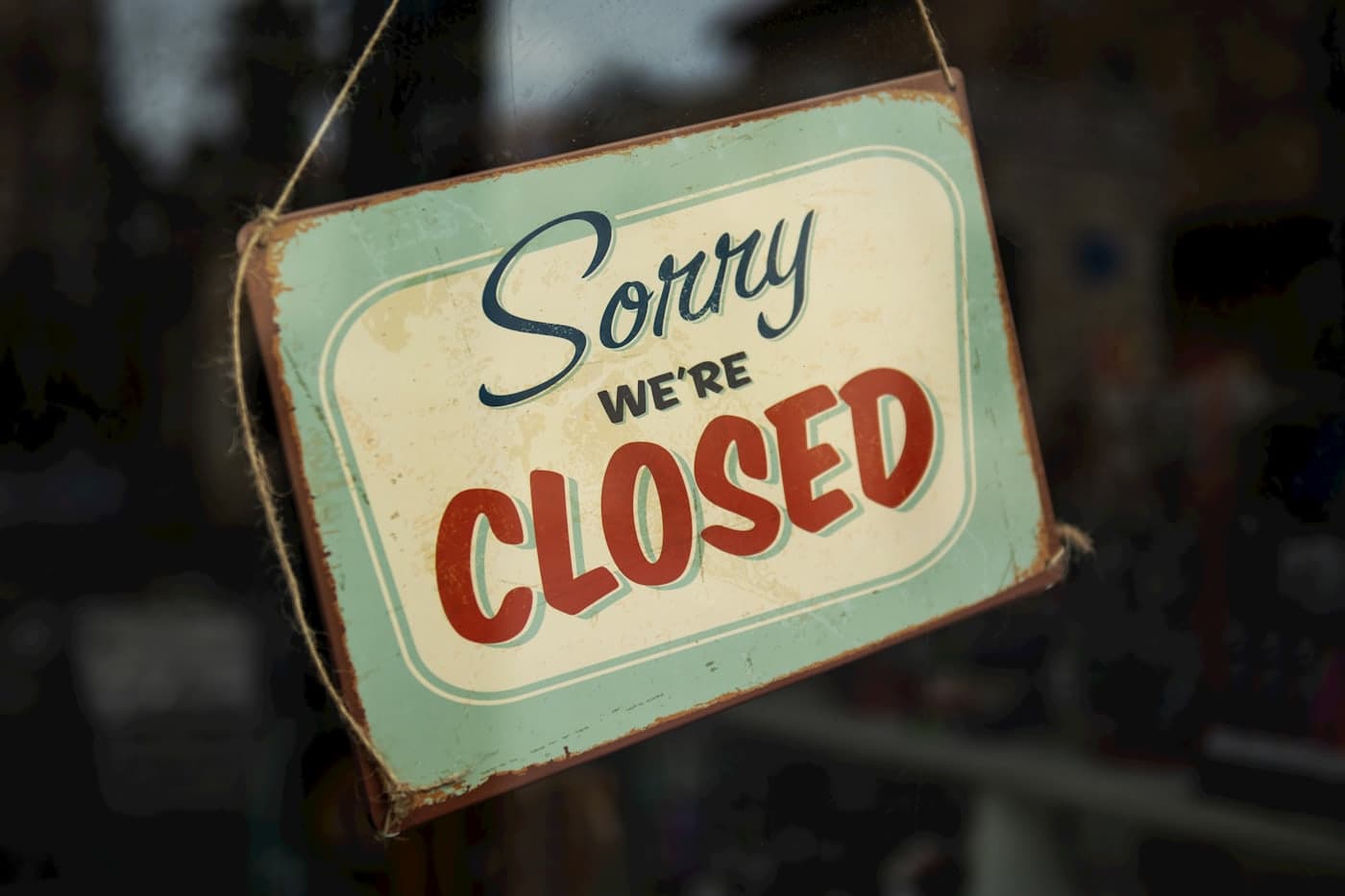 A vintage sign hanging in a shop window reading sorry, we're closed.