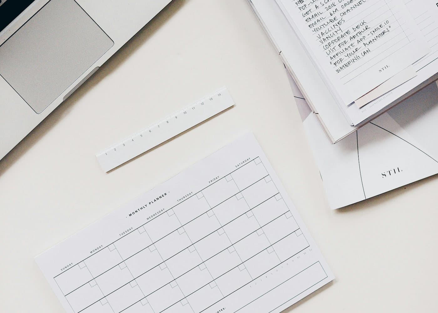 A tidy white desk with a laptop, a monthly planner page and handwritten to-do lists.