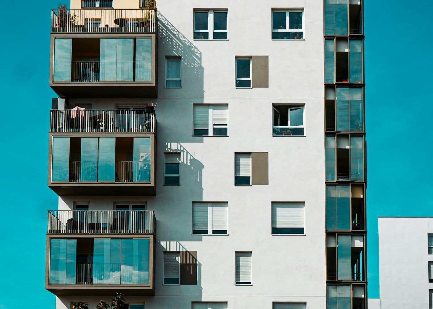 The glass balconies and facade of a modern apartment tower against a blue sky.