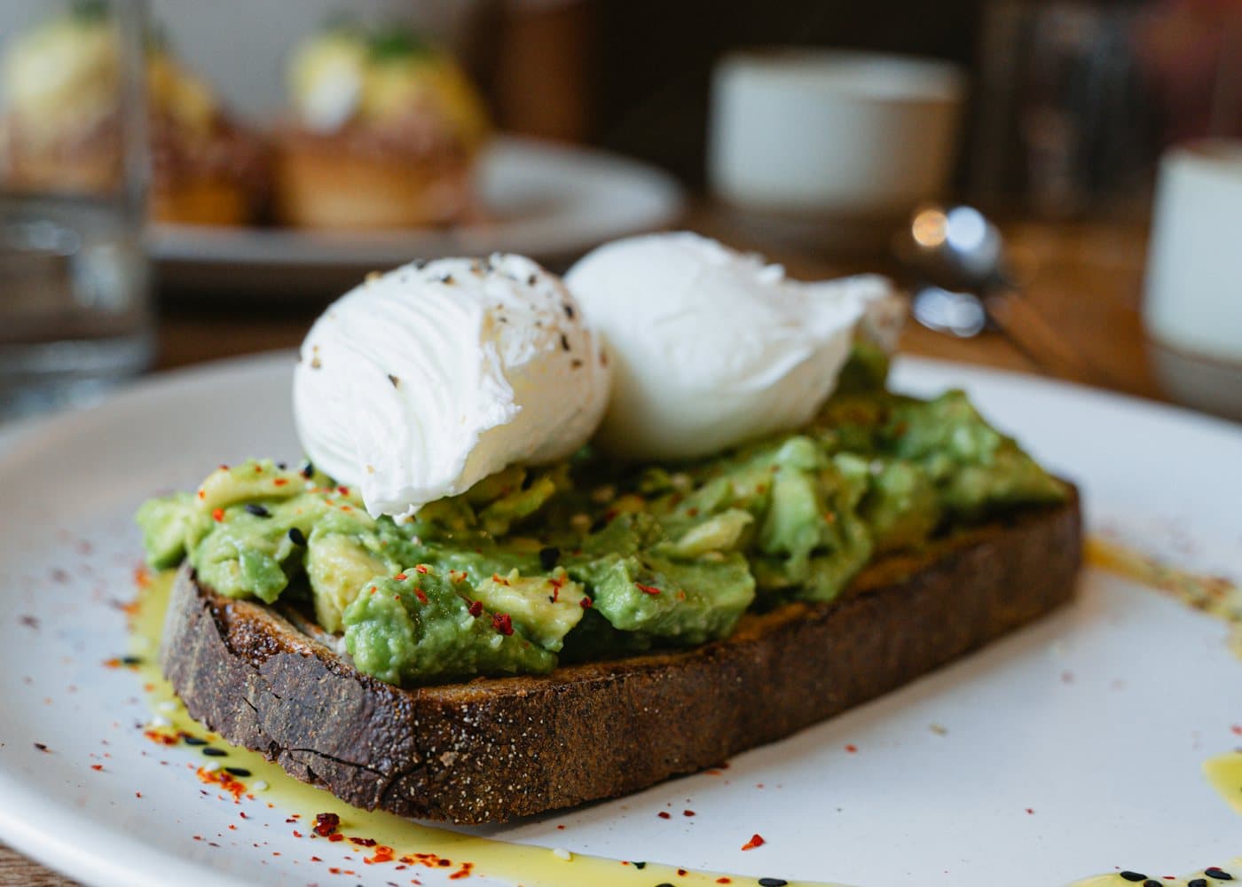 Smashed avocado toast with poached eggs on a cafe plate.