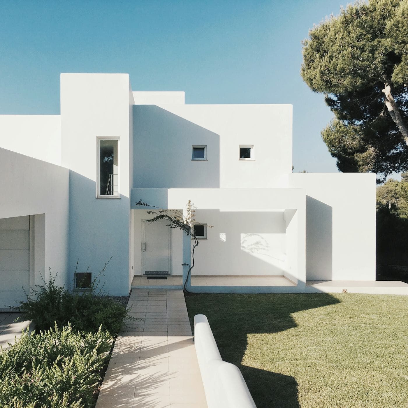 A modern white two-storey rental property with a lawn and mature tree.
