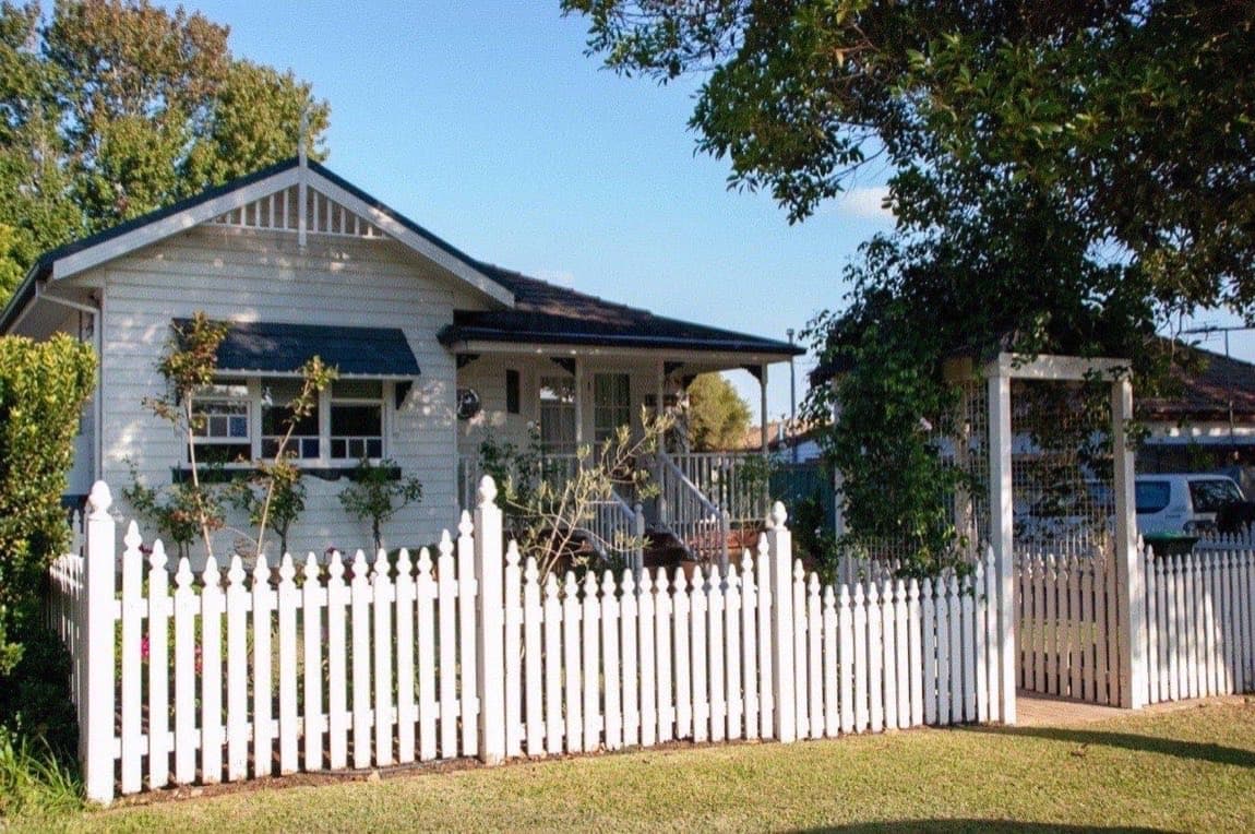 A weatherboard Australian rental house behind a white picket fence on a sunny day.